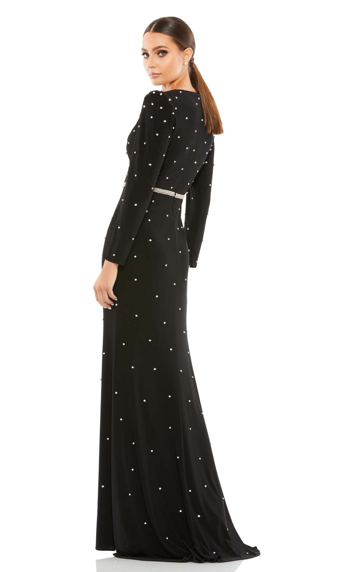 Woman in the Long Formal Dress 67874 by Mac Duggal, featuring pearl-like embellishments, a slim belt, and long sleeves, stands looking over her shoulder against a white background.